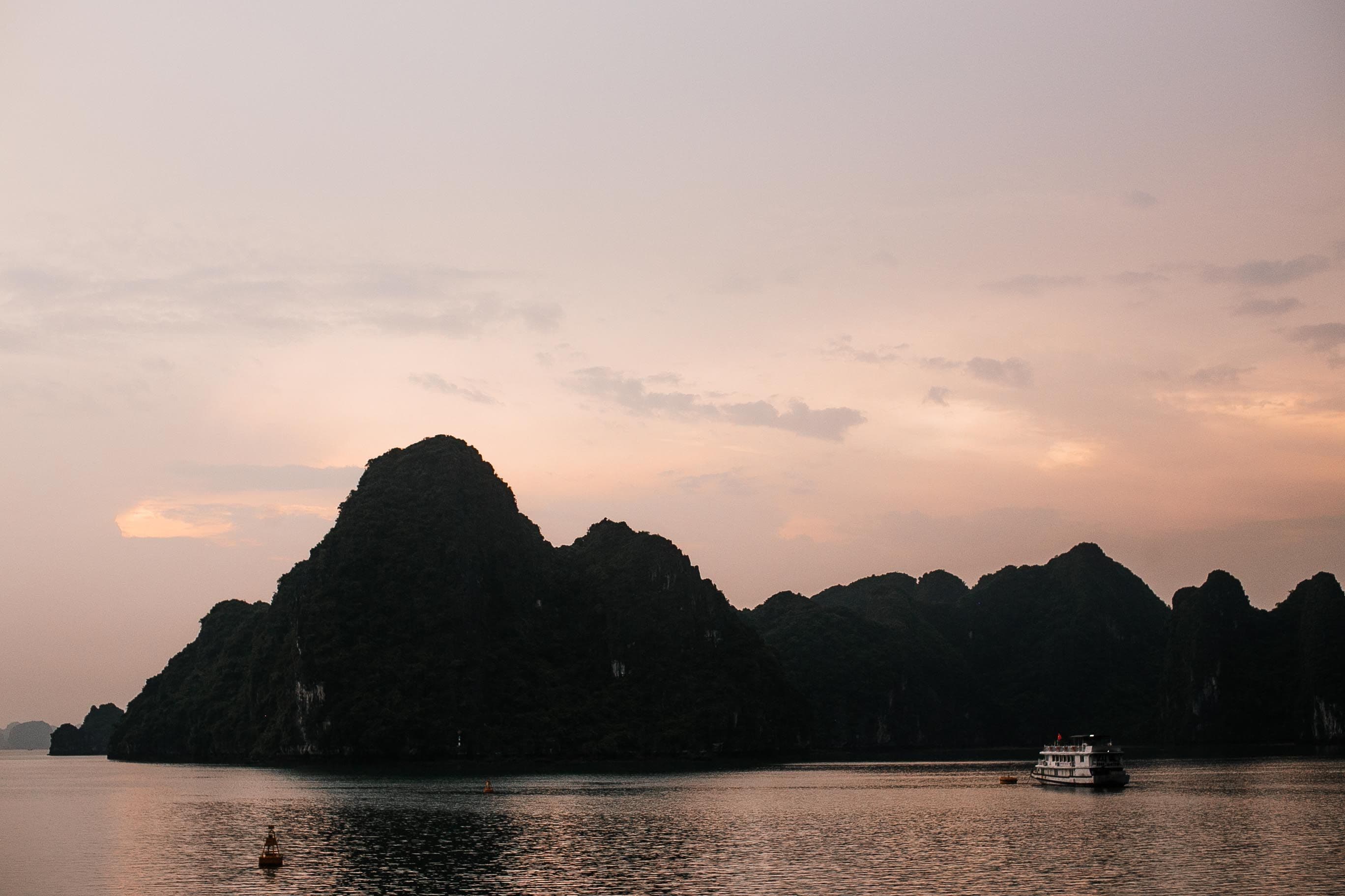 Limestone islands and a boat beneath a rose-coloured sunset in Ha Long Bay, Vietnam